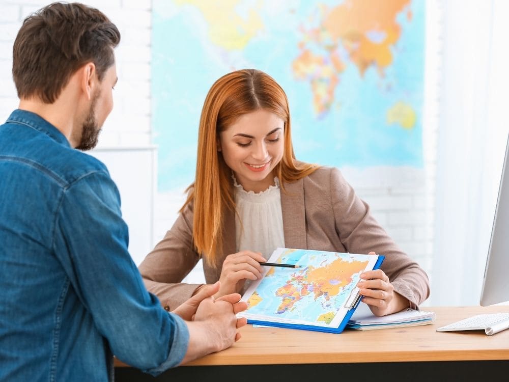 Conseillère en agence de voyage présentant un itinéraire à un client avec un carnet PDF de voyage